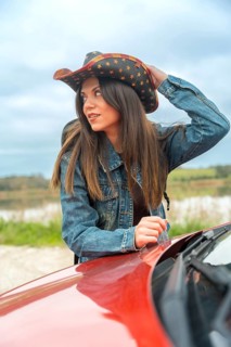 Vertical portrait of a distracted traveler leaning on a red car in the middle of a road