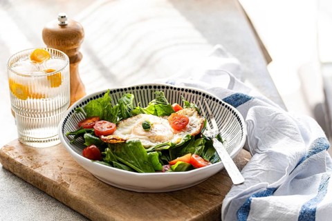 Top view of a healthy lunch featuring fresh spinach leaves, cherry tomatoes, and a fried egg in a