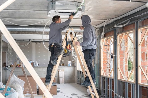 Air conditioning technicians are installing an hvac unit on the ceiling of a new building, standing