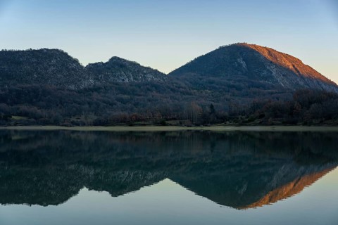 Picturesque view of mountains bathed in sunset light, reflected in a tranquil lake, surrounded by