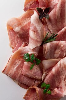 Raw bacon, sliced, with micro greenery and spices, on a white background, close-up