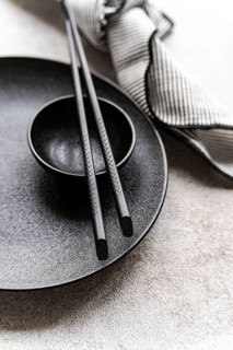 A minimalist black and white table setting featuring chopsticks on a textured plate, complemented
