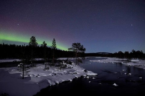 Aurora borealis in green colors over lake in snow covered landscape at night, Lapland, Finland