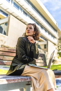 Vertical photo of an arab woman entrepreneur working with laptop outdoors sitting on bench