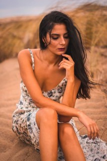 Portrait of a brunette Caucasian caressing her hair in a white floral dress, sitting on the sand on