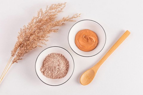 Top view of pink cosmetic clay powder and prepared facial mask in bowls with a decorative grass
