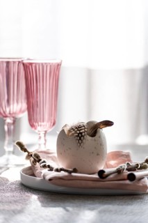A stylish Easter dining setup with a focal decorative egg adorned with feathers, nestled on a