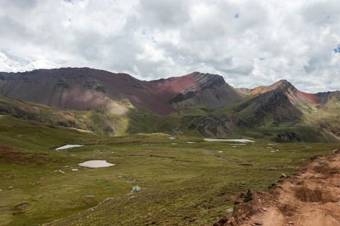 Lush green meadows and sparse glacial lakes set against the dramatic backdrop of the Ausangate