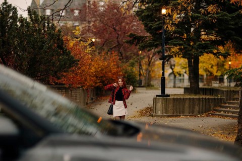 A woman in a red plaid jacket poses joyfully on a Montreal street, surrounded by vibrant autumn