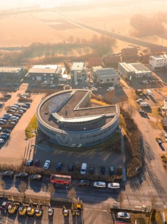 Round industrial building with parked cars and surrounding streets from aerial view in sunny
