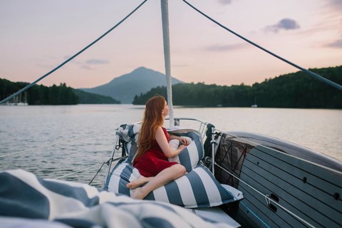 A person in a red dress relaxes on cushions aboard a sailboat, enjoying a peaceful, scenic