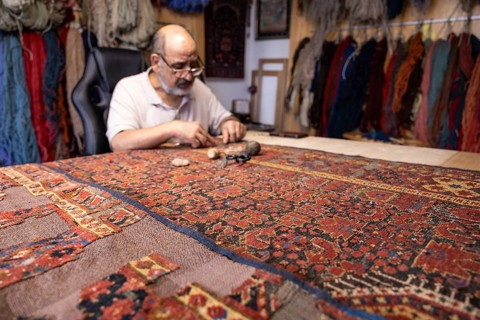 A senior senior male Iranian carpet restorer carefully repairs a traditional rug in his Salzburg