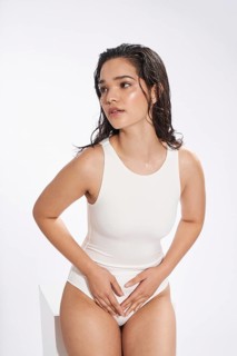 A young female model, looking away from the camera, poses in a studio setting, dressed in a simple
