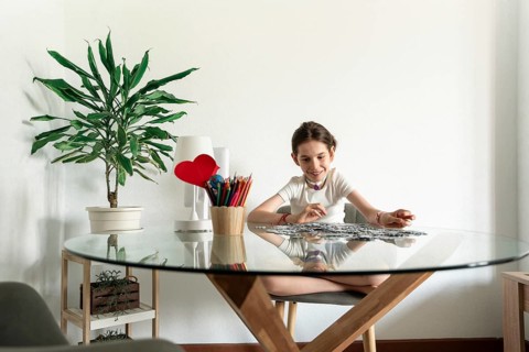 A disabled girl with a tracheostomy sits at a table, focusing on a puzzle. Surrounded by art