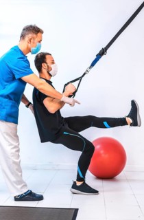 Physiotherapist with mask and a patient doing stretches with rubber bands. Physiotherapy with