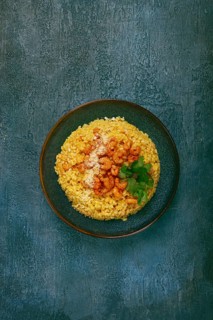Risotto with shrimp, in a bowl, on a textured surface, with a side dish of fresh coriander,