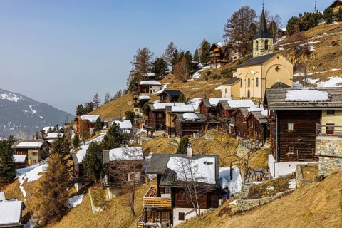 Snow-covered old farmhouses, back the Sainte Barbe Baroque Church, Historic Town Center, Chandolin,