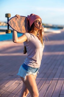 Confident young woman holding a skateboard over her shoulder, enjoying a sunny day by the