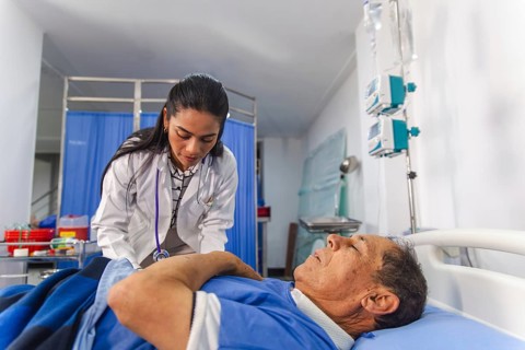 A female doctor attentively examines an elderly male patient in a hospital setting. The room is