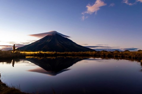 Side view of unrecognizable person admiring the tranquil reflection of Mount Taranaki in a serene