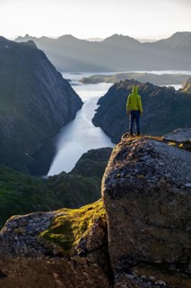 Mountaineer, young man standing on rocks and looking into the distance, at sunrise, fjord
