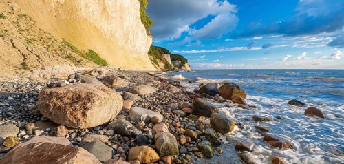 Chalk cliffs and rocky beach with boulders on the Baltic Sea under blue sky with cumulus clouds,