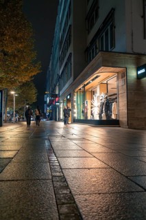 Night-time street scene with illuminated shop windows, wet pavement and autumnal atmosphere,