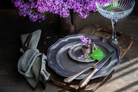 Elegant table setting with vintage plates, delicate lilac flowers in a tin cup, and a graceful