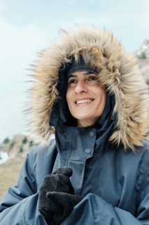 A cheerful woman wearing a thick winter coat with a fur-lined hood, smiling while enjoying the cold