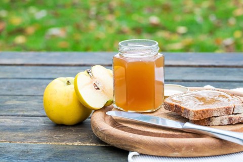A rustic breakfast scene on a wooden table featuring a jar of quince jam, a knife, sliced bread