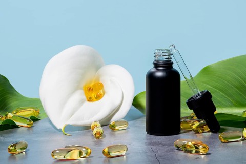 Mat black bottle of cosmetic serum next to a white white calla lily, featuring a pipette and