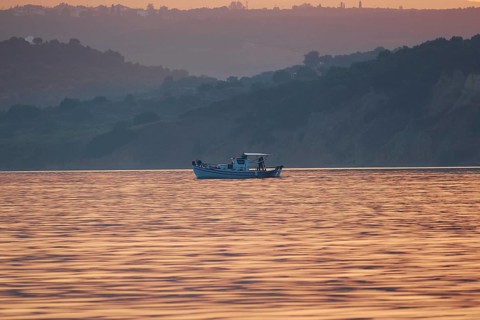 Fishing boat on pastel-colored water in front of a hilly landscape at sunrise, Navarino Bay, Pylos,
