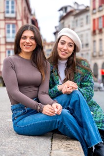 Two cute chic friends smiling at camera sitting in the city street