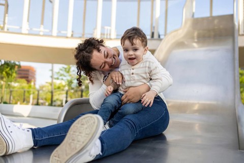 A joyful moment captured as a mother and her baby sit together on a slide at the park. The sun