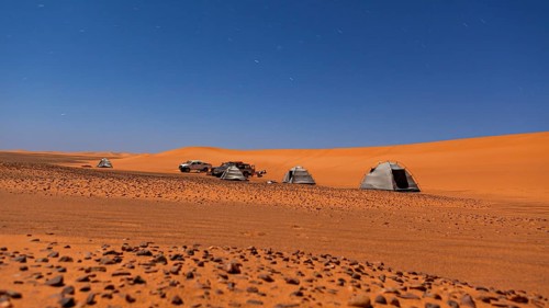 Tents and cars standing in a vast desert under a clear night sky, tent camp in the Sahara desert
