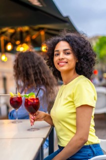 Vertical photo of a latin woman smiling at camera while enjoying cocktails with friends in an