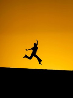 A dynamic silhouette of a woman jumping energetically against a vibrant orange sunset in