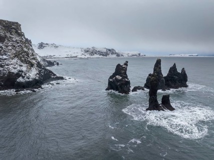 Stunning sea stacks rise from the ocean along Vik's snowy coastline in Iceland. Capturing nature's