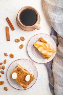 Honey cake with milk cream, caramel, almonds and a cup of coffee on a white concrete background and