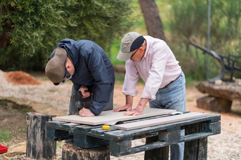 A senior father and his adult son bond while working on a carpentry project outdoors. Both men are