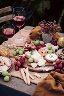 An elegant setting with a cheese board, assorted grapes, breadsticks, and cold cuts. Two glasses of