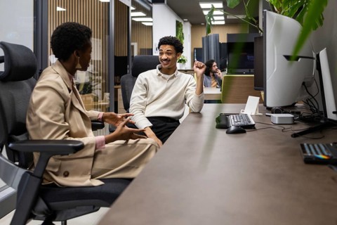 Two colleagues converse in a modern office setting, sitting across from each other. The environment