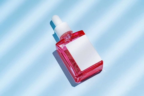 Top view of a red cosmetic serum bottle with a white label, set against a textured blue background,