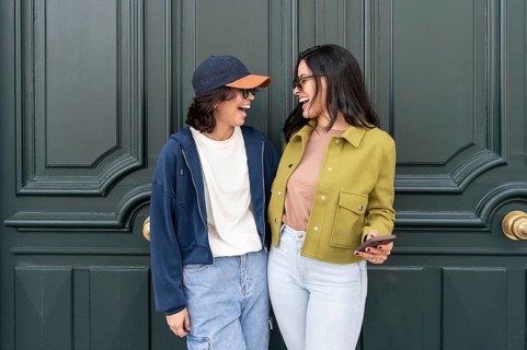 A happy lesbian couple shares a joyful moment outdoors, laughing together. They are dressed