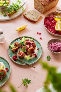 A vibrant Mediterranean meal featuring meatballs, pomegranate seeds, yogurt, sliced cucumbers, and