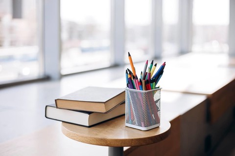 Colorful stationery items such as pencils and pens in a mesh holder alongside two hardcover books