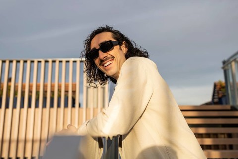 A fashionable man with sunglasses and a mustache relaxes on a sunny outdoor terrace His casual