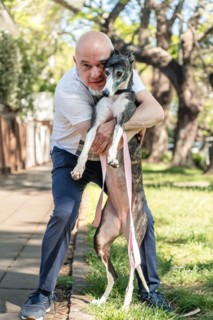 Vertical shot of a man embracing his greyhound pet, both looking at the camera while strolling down