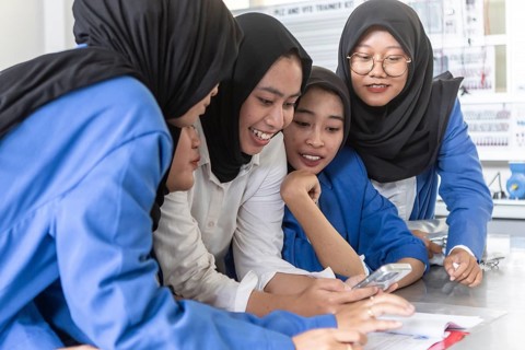 Asian Muslim teacher engaging with students using a smartphone in a classroom setting. The
