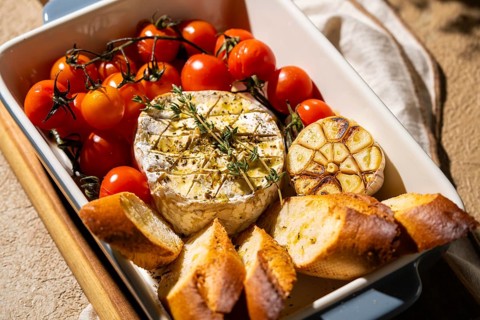 Savory baked Camembert surrounded by cherry tomatoes, roasted garlic, and crispy bread slices in a
